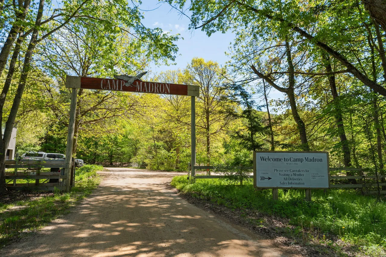 The Camp Madron entrance gate under a canopy of spring trees
