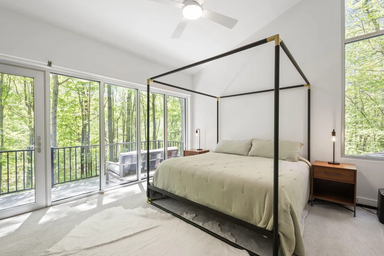 A four-post bed in a bright room with floor-to-ceiling windows onto the forest