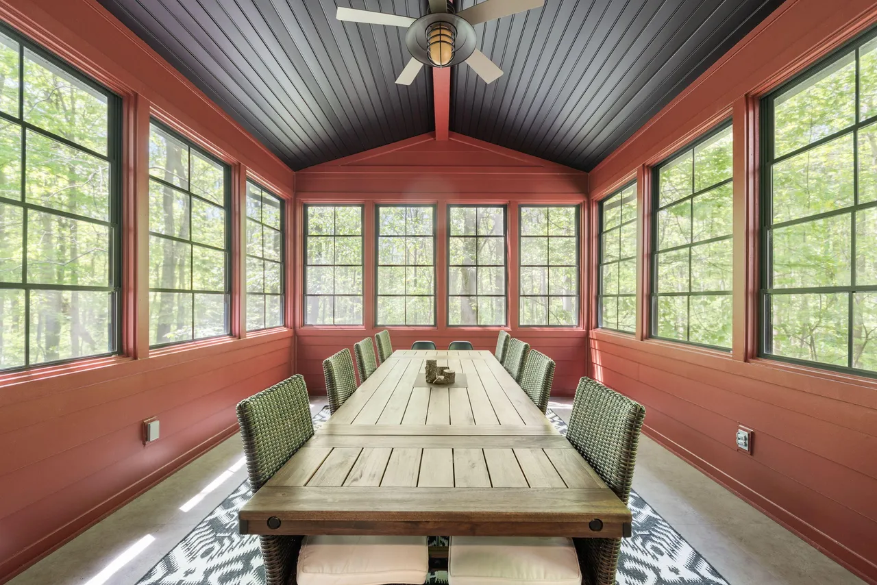 A long dining table surrounded by windows overlooking the forest