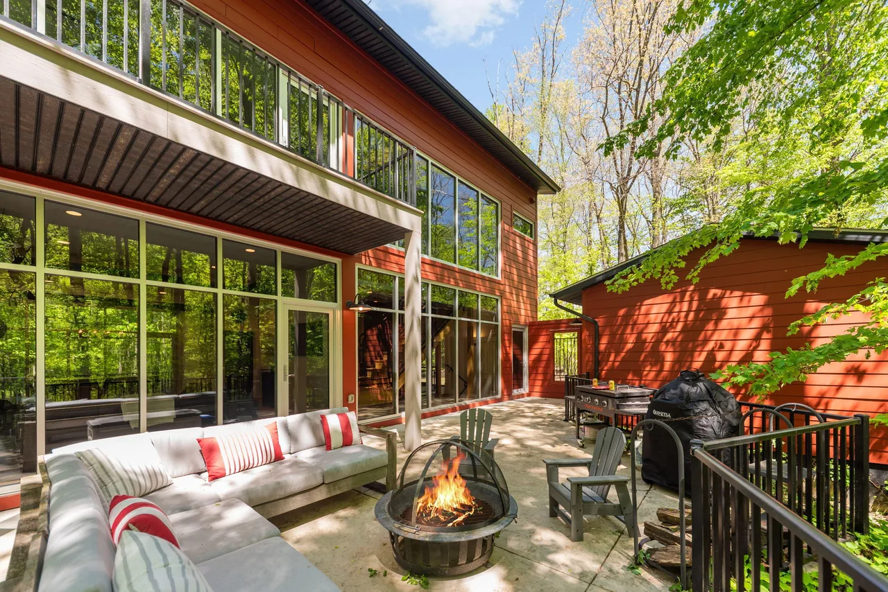 Patio with a fire pit, outdoor sofa, and large glass walls looking into the woods