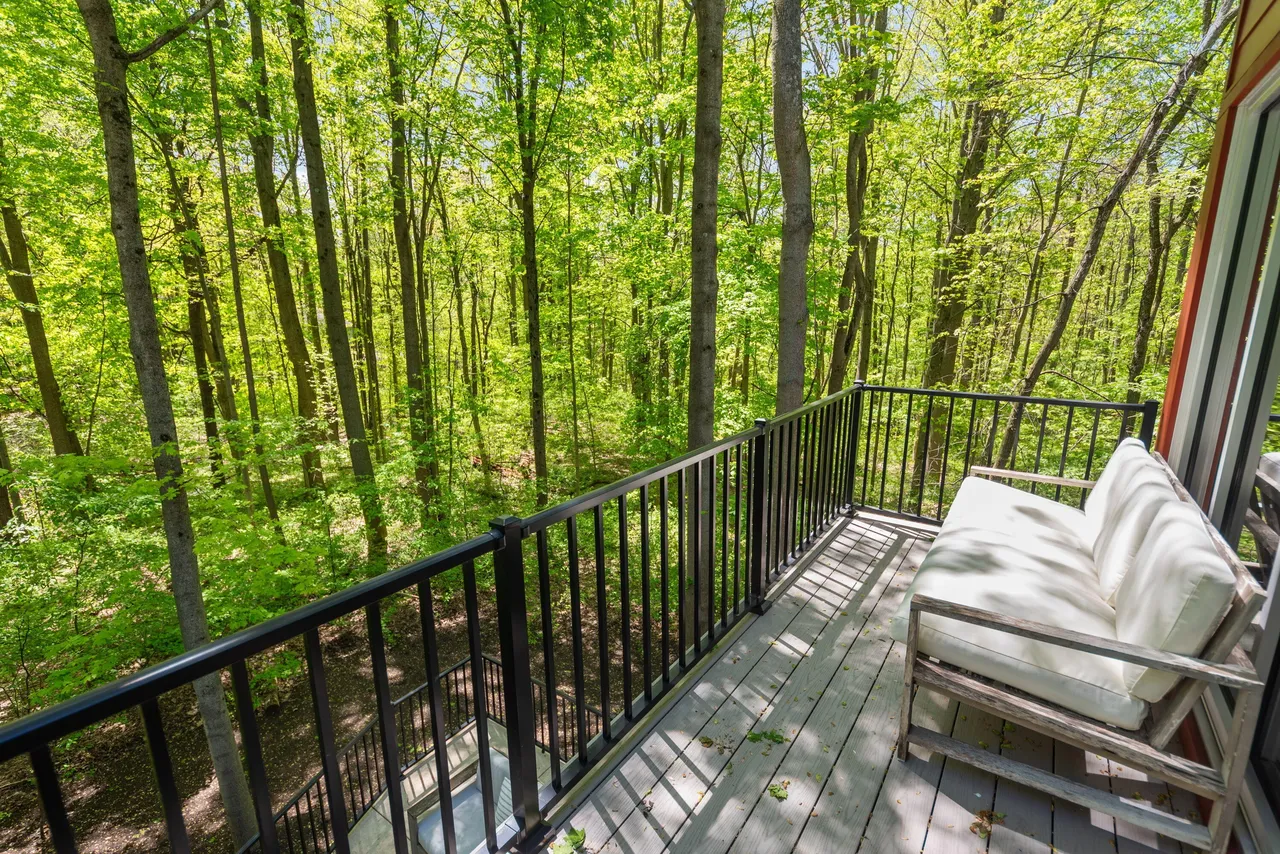 A sofa on a balcony surrounded by tall Michigan hardwood trees